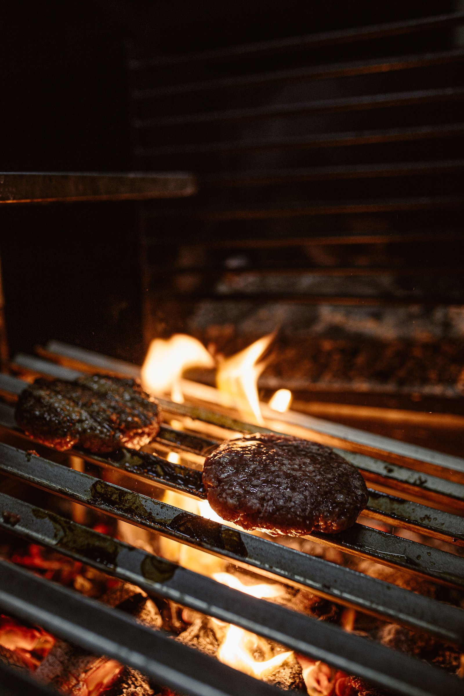 Burger patty grilling over open flame